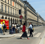 Woman in a red jacket crossing a Parisian street with a crowd in the background